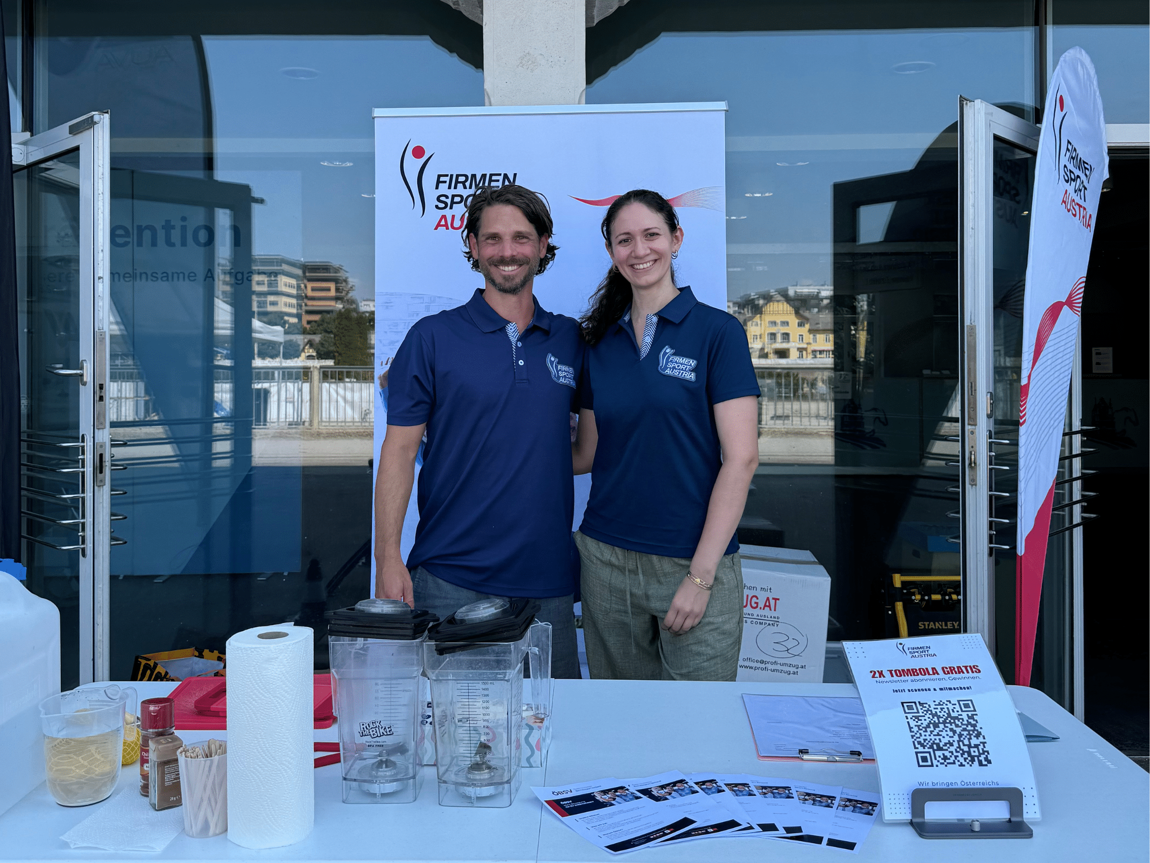 Mitarbeitende von Firmen Sport Austria begrüßen Besucherinnen und Besucher am Informationsstand.